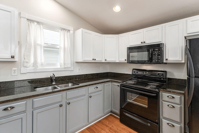 kitchen featuring lofted ceiling, a sink, dark stone countertops, light wood-type flooring, and black appliances