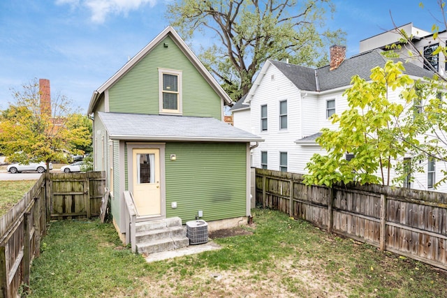 rear view of property with entry steps, central air condition unit, a fenced backyard, and a yard