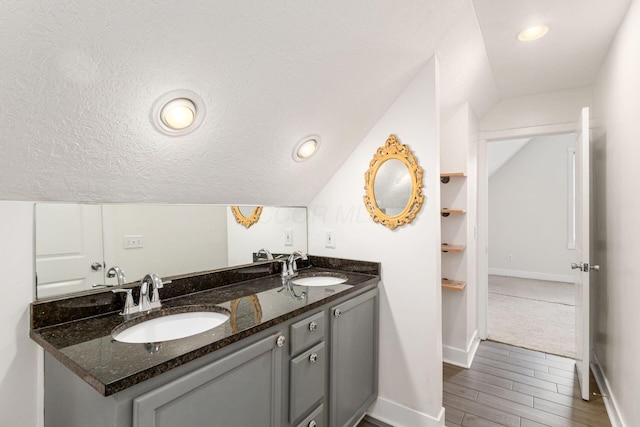 bathroom with double vanity, a textured ceiling, vaulted ceiling, and a sink