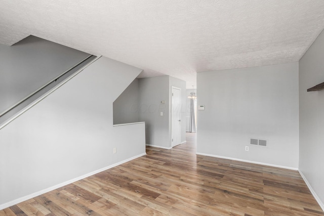 empty room featuring baseboards, a textured ceiling, visible vents, and wood finished floors