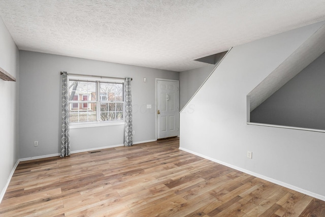 empty room with a textured ceiling, baseboards, and wood finished floors