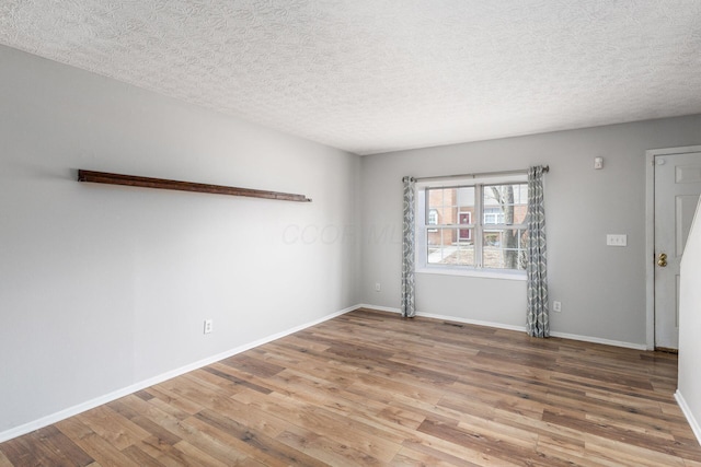 empty room featuring a textured ceiling, wood finished floors, and baseboards