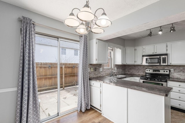 kitchen with stainless steel appliances, a peninsula, a sink, decorative backsplash, and dark countertops