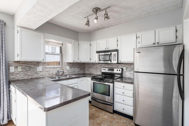 kitchen featuring dark countertops, a peninsula, stainless steel appliances, and a sink