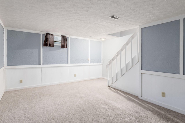 carpeted spare room with a textured ceiling, a textured wall, a wainscoted wall, visible vents, and stairway