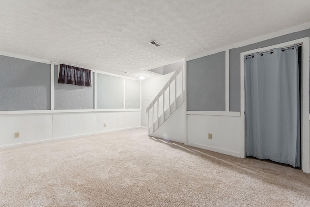 carpeted empty room featuring a textured ceiling, baseboards, and stairs