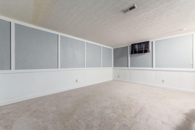 carpeted empty room featuring a textured ceiling and visible vents