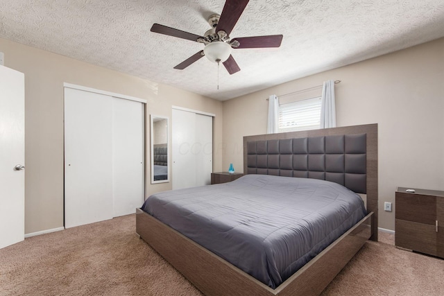 bedroom with two closets, a textured ceiling, a ceiling fan, and carpet flooring