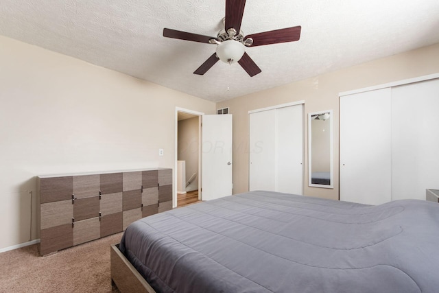 carpeted bedroom featuring a ceiling fan, visible vents, a textured ceiling, and two closets