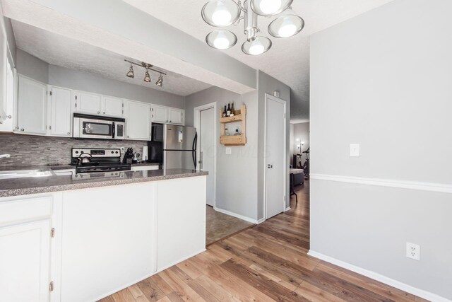 kitchen featuring light wood-style flooring, stainless steel appliances, a peninsula, a sink, and white cabinetry