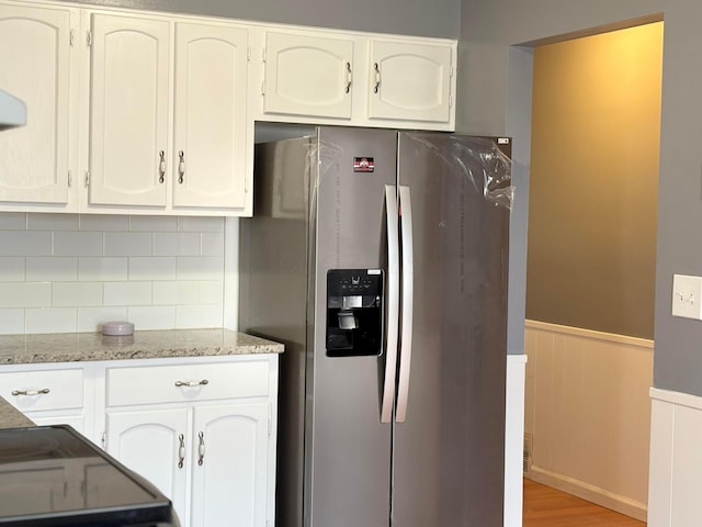 kitchen featuring light stone counters, a wainscoted wall, light wood-style floors, stainless steel refrigerator with ice dispenser, and white cabinetry