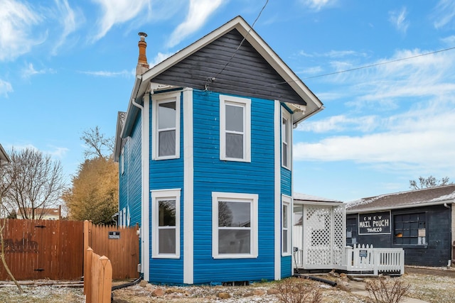 rear view of house featuring a chimney and fence