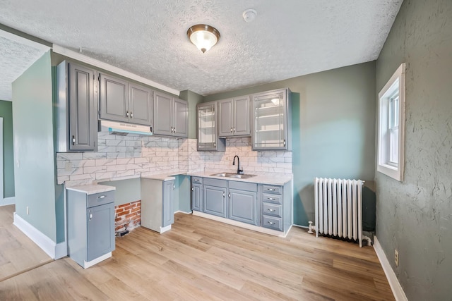 kitchen with radiator heating unit, gray cabinets, a sink, and light wood-style flooring