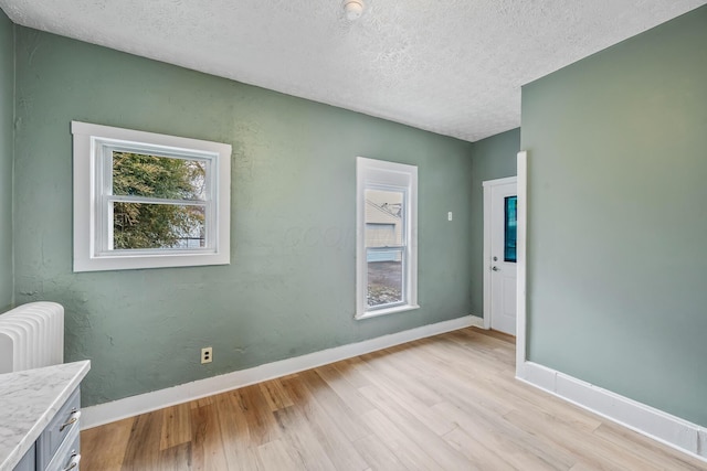 spare room with light wood-type flooring, baseboards, and a textured ceiling