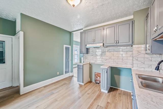 kitchen featuring light wood-style floors, gray cabinets, a sink, and backsplash