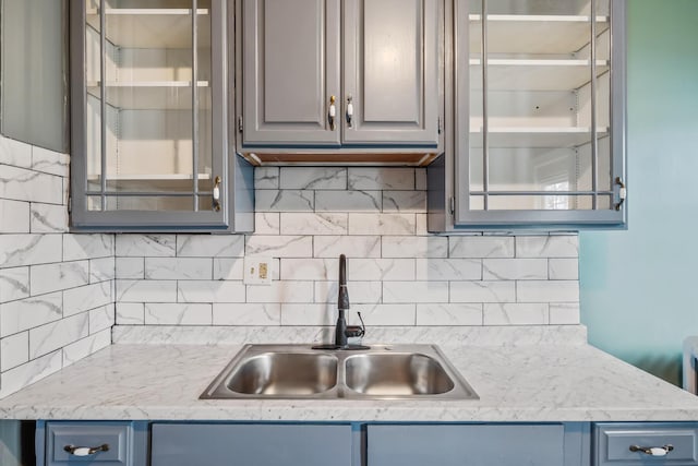 kitchen with gray cabinets, glass insert cabinets, decorative backsplash, and a sink