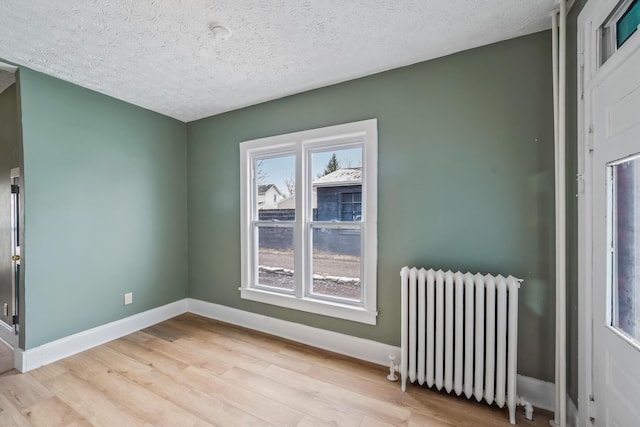 unfurnished room featuring baseboards, a textured ceiling, light wood-type flooring, and radiator