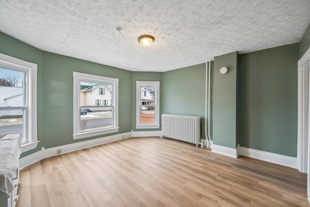 spare room featuring baseboards, a textured ceiling, radiator heating unit, and wood finished floors