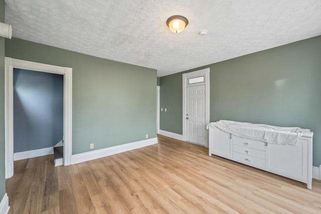 empty room featuring light wood-style floors, a textured ceiling, and baseboards