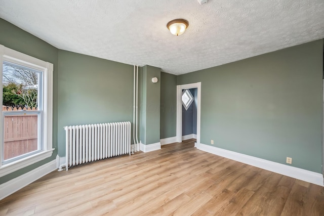 empty room featuring radiator heating unit, a textured ceiling, baseboards, and wood finished floors