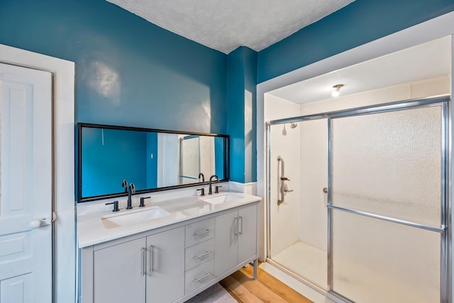 full bathroom with a sink, a shower stall, a textured ceiling, and double vanity