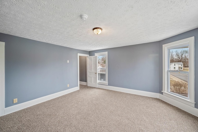 empty room with carpet, baseboards, and a textured ceiling