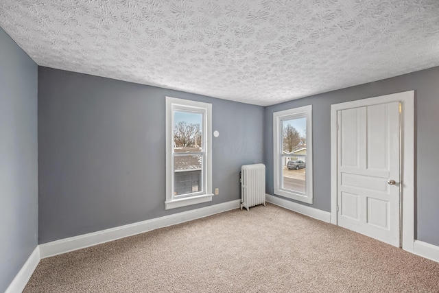 empty room with baseboards, a textured ceiling, carpet flooring, and radiator