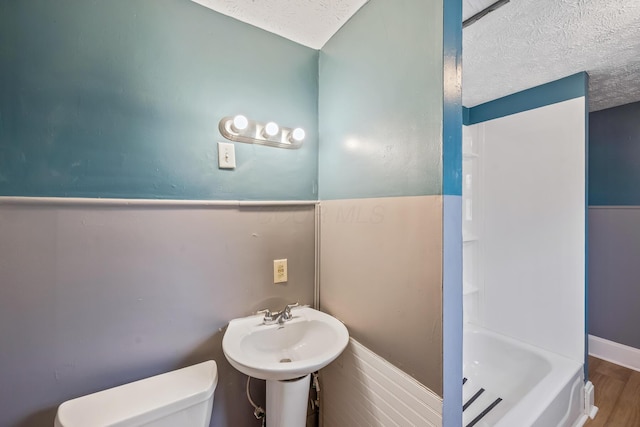 bathroom with a shower, toilet, wood finished floors, a textured ceiling, and a sink