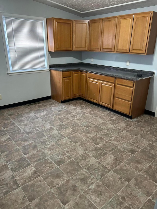 kitchen with dark countertops, baseboards, brown cabinetry, and a textured ceiling