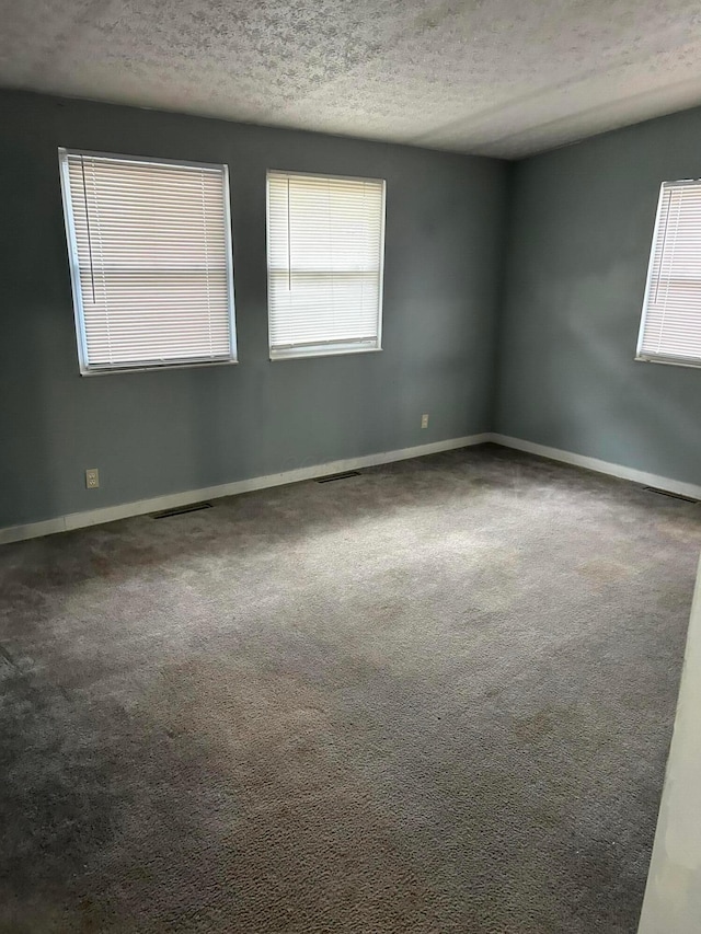 carpeted spare room featuring visible vents, a textured ceiling, and baseboards