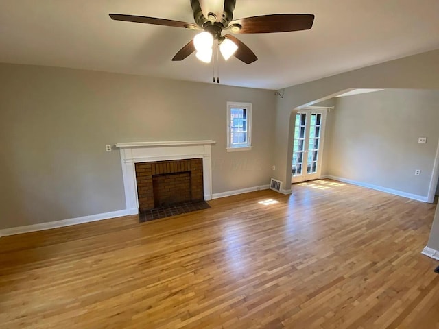 unfurnished living room with light wood finished floors, a brick fireplace, and baseboards