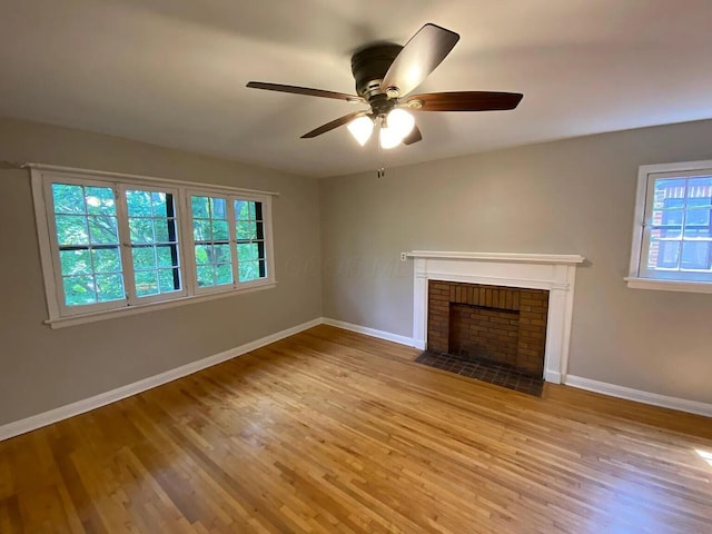 unfurnished living room with a brick fireplace, wood finished floors, baseboards, and ceiling fan