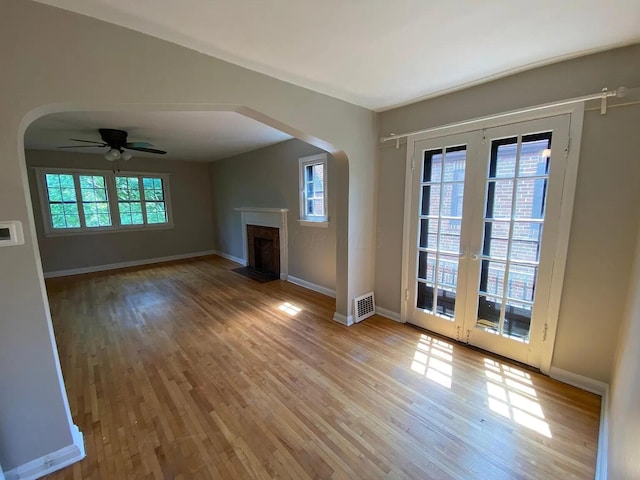 unfurnished living room featuring a fireplace with flush hearth, wood finished floors, visible vents, and arched walkways