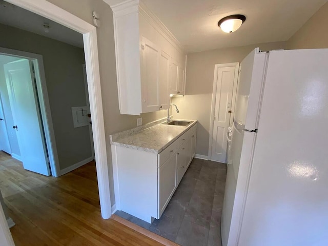 kitchen featuring baseboards, light countertops, freestanding refrigerator, white cabinetry, and a sink