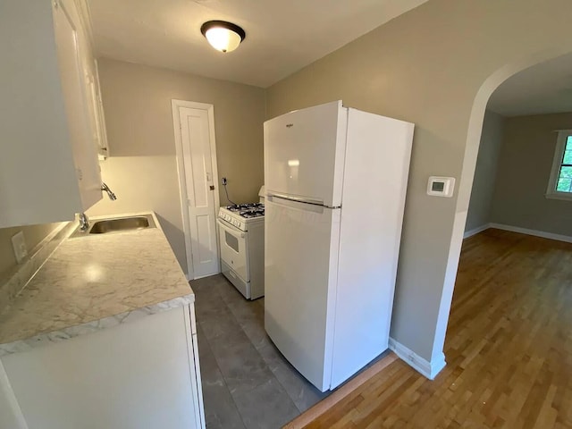 kitchen featuring white appliances, baseboards, arched walkways, a sink, and light countertops