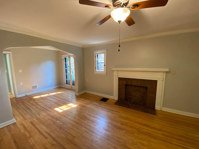 unfurnished living room featuring visible vents, arched walkways, wood finished floors, and crown molding