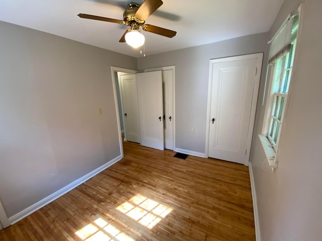 unfurnished bedroom featuring ceiling fan, visible vents, baseboards, and wood finished floors