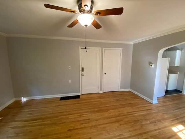 spare room with a ceiling fan, arched walkways, crown molding, light wood finished floors, and baseboards