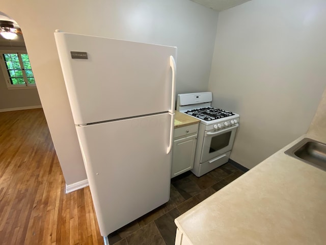 kitchen featuring a sink, white appliances, light countertops, baseboards, and dark wood-style flooring