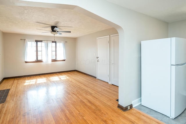 empty room featuring visible vents, baseboards, light wood-style floors, arched walkways, and a textured ceiling