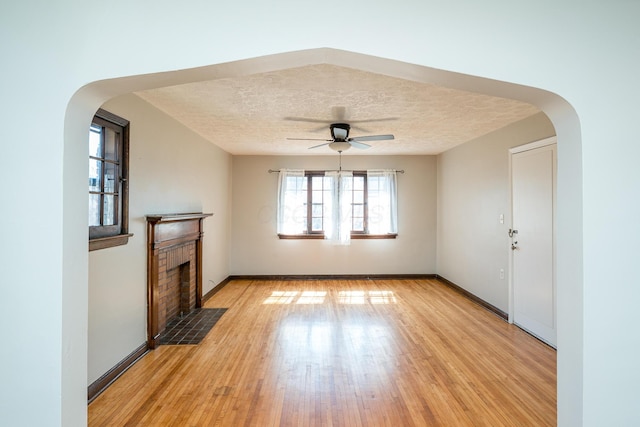 unfurnished living room with light wood-type flooring, arched walkways, a textured ceiling, and a brick fireplace