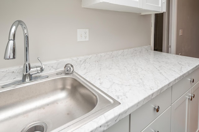 interior details featuring a sink, light stone counters, and white cabinets