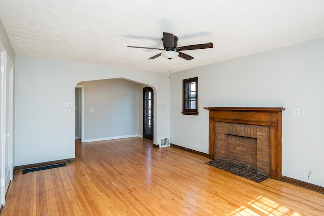 unfurnished living room with light wood-type flooring, visible vents, arched walkways, baseboards, and a brick fireplace