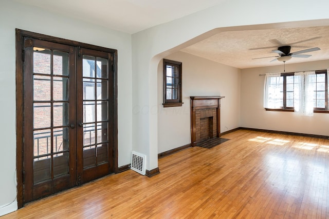 unfurnished living room featuring visible vents, baseboards, a brick fireplace, and light wood finished floors