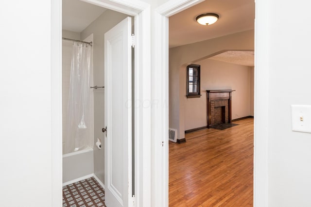 full bathroom featuring visible vents, wood finished floors, shower / tub combo, baseboards, and a brick fireplace