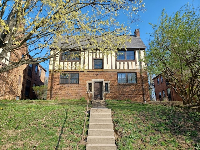 english style home featuring brick siding, a front lawn, a shingled roof, and a chimney