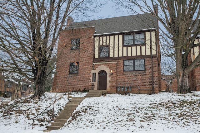 tudor house with a shingled roof, brick siding, a chimney, and stucco siding