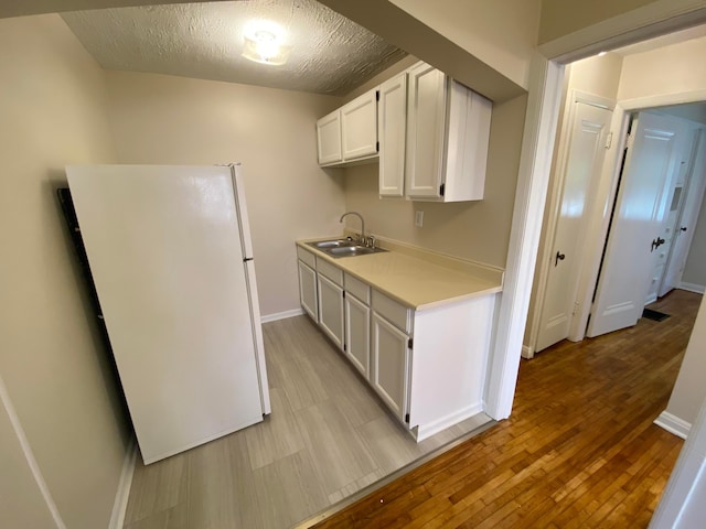 kitchen with light countertops, freestanding refrigerator, white cabinets, a sink, and light wood-type flooring