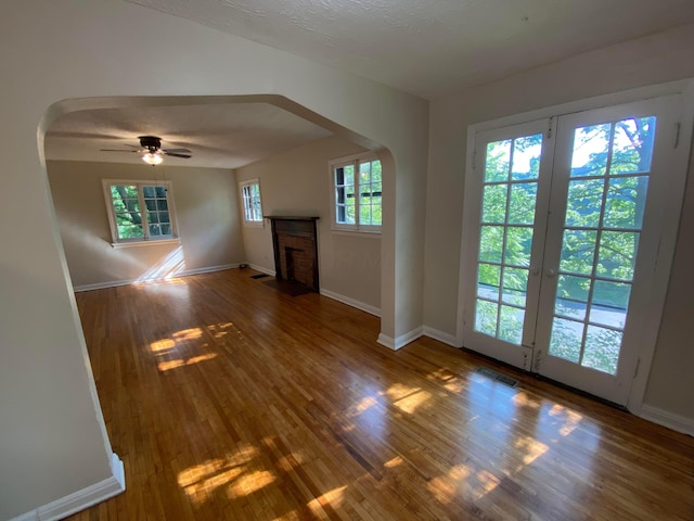 unfurnished living room with arched walkways, a fireplace, visible vents, baseboards, and wood-type flooring