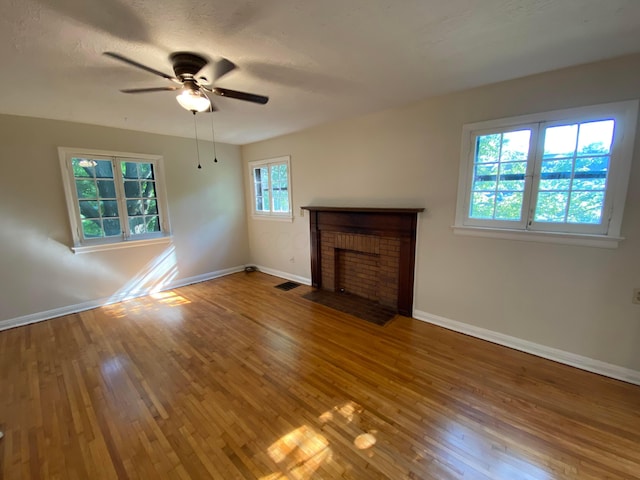 unfurnished living room with a ceiling fan, baseboards, visible vents, a brick fireplace, and wood-type flooring